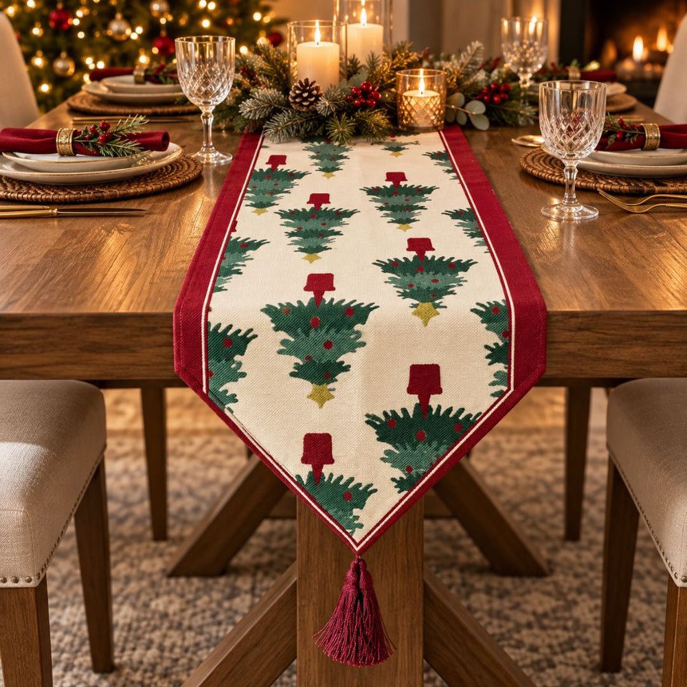 Camino de mesa navideño beige con árboles verdes y borlas rojas.