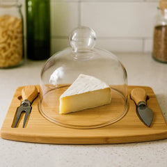 Tabla de queso con domo de vidrio y utensilios al lado