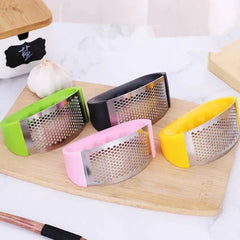 Machacador de ajo acero inoxidable con recubrimiento de silicona verde en tabla de cocina.