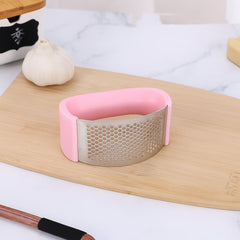 Machacador de ajo acero inoxidable con recubrimiento de silicona verde en tabla de cocina.