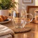 Vaso de vidrio transparente de 250 ml con doble pared, cámara de aire, diseño redondeado y asa lateral.