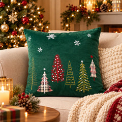Cojín navideño cuadrado verde de 43 × 43 cm con árboles de Navidad multicolor, detalles decorativos y copos de nieve blancos.
