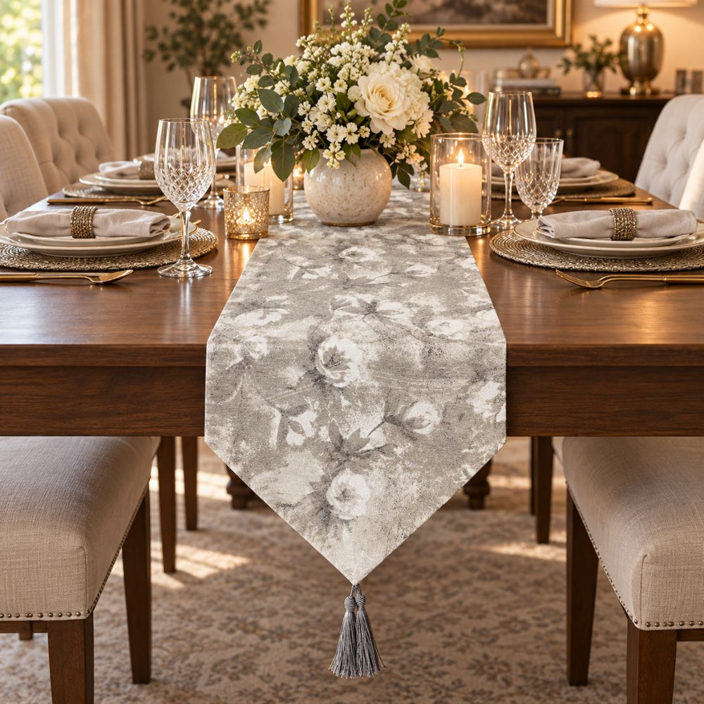 Camino de mesa gris plata y blanco con diseño floral y borla decorativa.