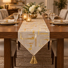 Camino de mesa beige con cuadros dorados y extremo triangular con borla decorativa.