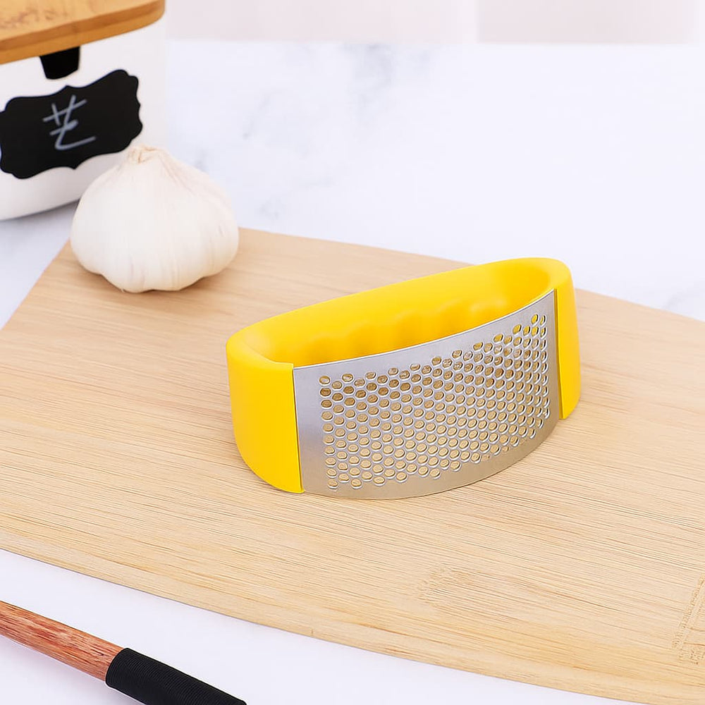 Machacador de ajo acero inoxidable con recubrimiento de silicona verde en tabla de cocina.